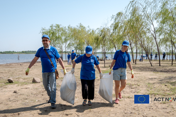 3 volunteers on the beach, holding trash bags for cleaning.